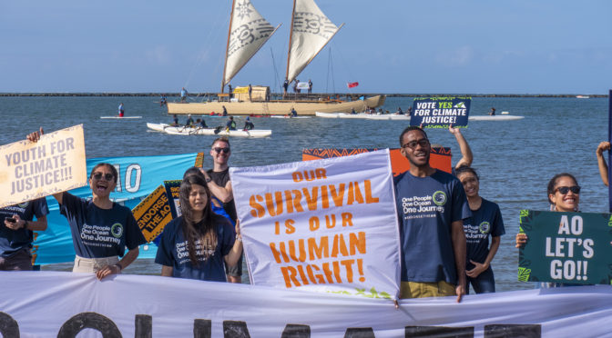 Image showing young people holding climate protest signs in front of an ocean with canoes