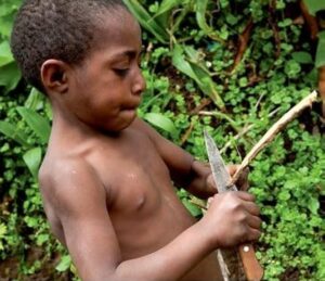 A young African boy uses a knife to carve a stick